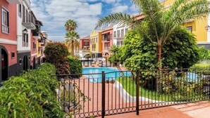 Una piscina rodeada de edificios coloridos, una zona cercada y abundante vegetación.