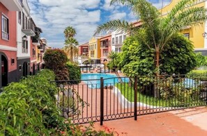 Ein Pool, umgeben von bunten Gebäuden, einem eingezäunten Bereich und üppiger Vegetation.