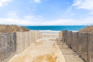 Ein Strandweg, der zum Meer führt, gesäumt von einem Holzzaun auf beiden Seiten.