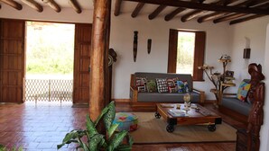 Amplia sala de estar con techo de madera, un sofá con cojines de colores, una mesa de centro con diversos objetos y una planta grande.