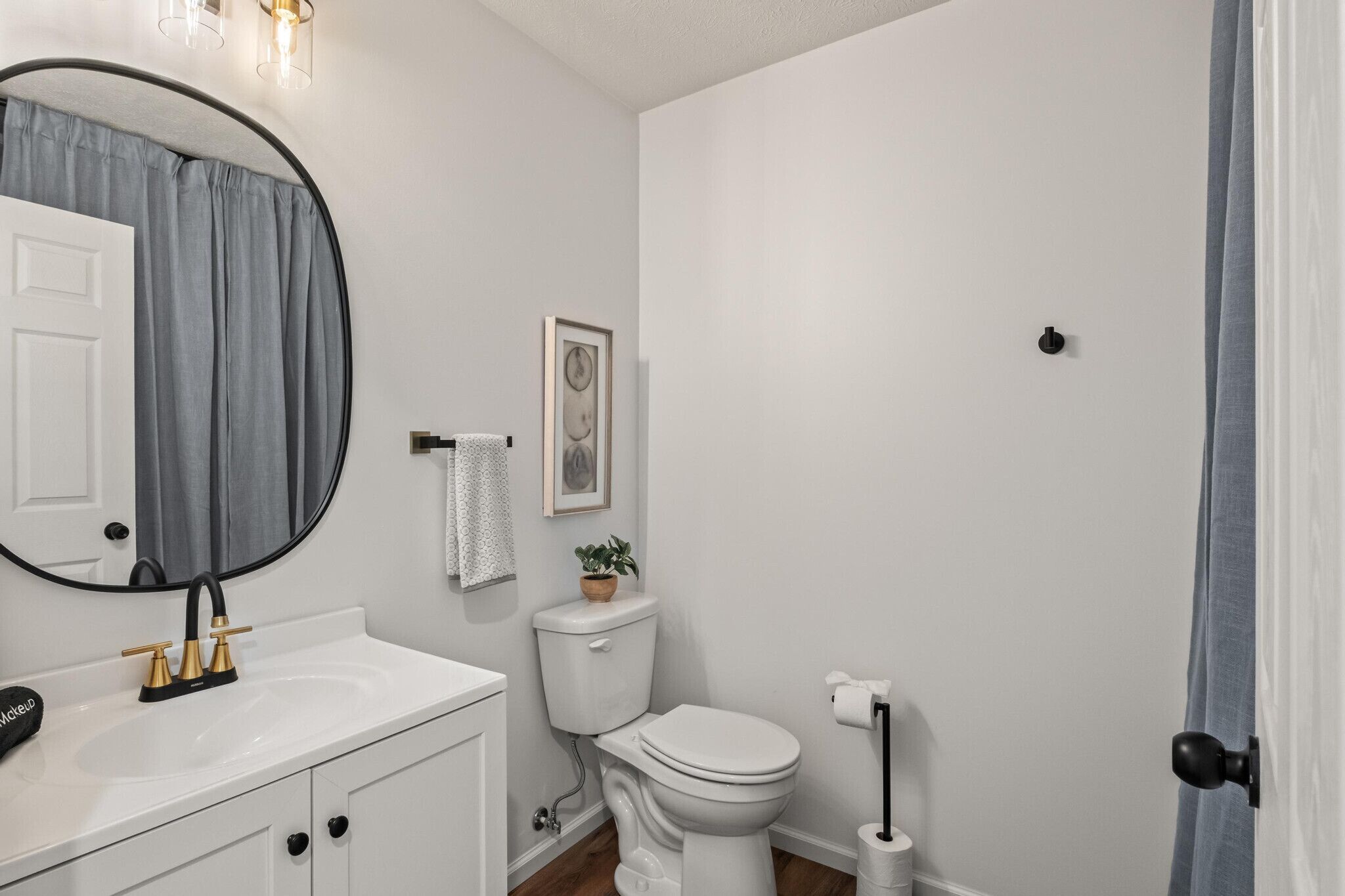 Een badkamer met een wit wastafel, toilet, spiegel en een lijst met een foto aan de muur.