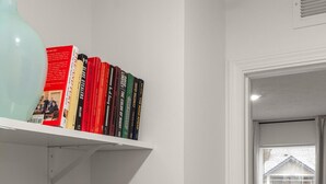 A room with a bookshelf, a potted plant, and a bed with a red blanket.