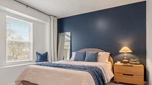 A bedroom with a bed, a nightstand, a lamp, and a window with blinds.