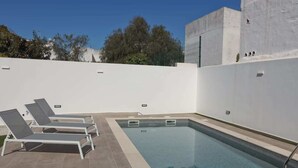 Piscina amb gandules, terrassa enrajolada i paret blanca.
