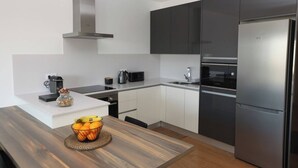 Una cuina moderna amb armaris blancs i foscos, electrodomèstics d'acer inoxidable i una taula de dinar de fusta amb un plat de fruita.