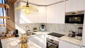 A modern kitchen with white cabinetry, a marble countertop, a built-in oven, a microwave, a coffee maker, and a hanging light fixture. - New cosy home & private garden -Near Paris - Free parking (Franconville)