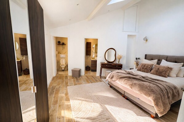 Une chambre avec un grand lit, une commode, un miroir et une vue sur la salle de bain.