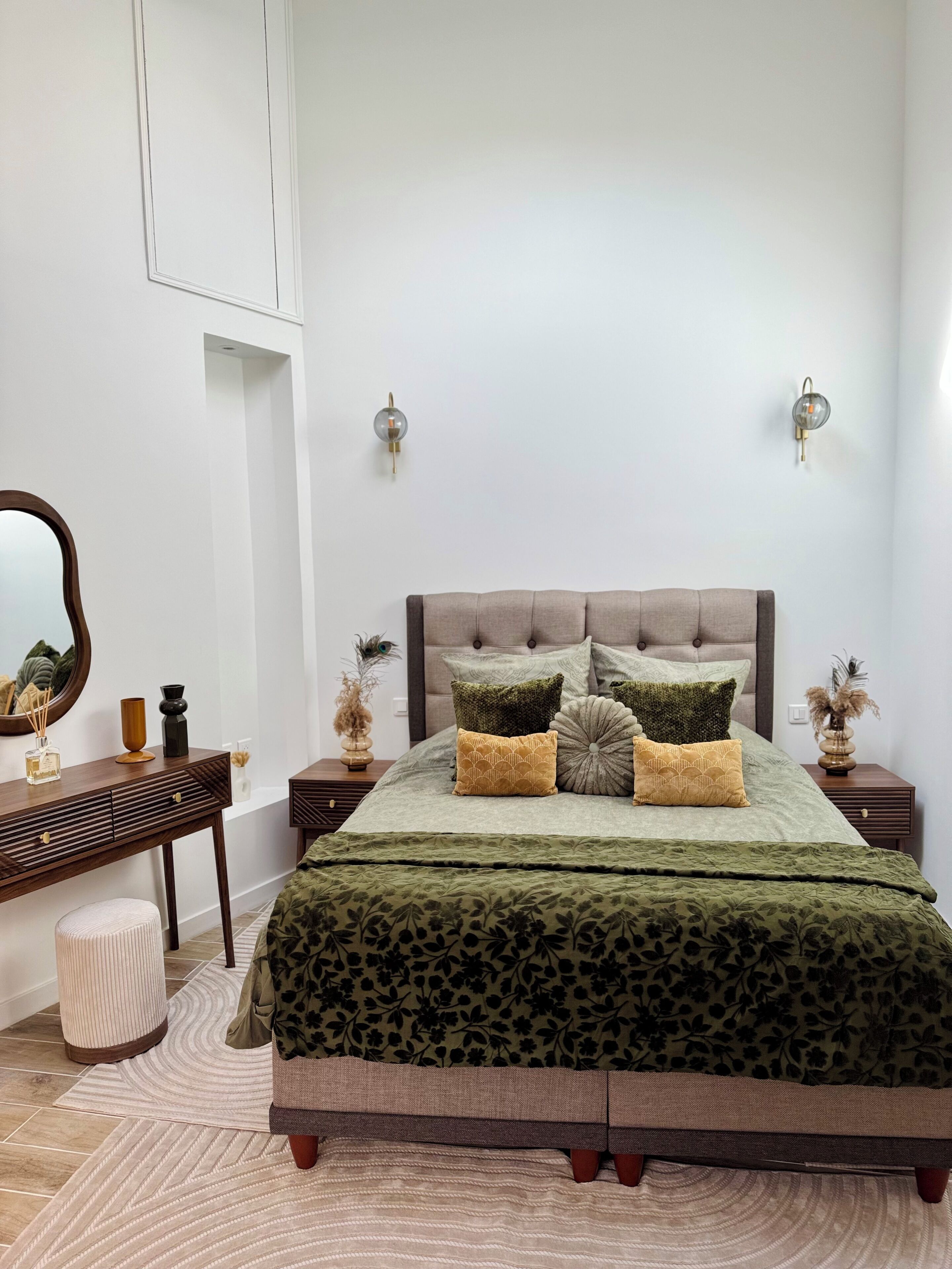 Un dormitorio con cama, mesitas de noche, cómoda, espejo y apliques de pared.