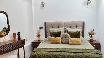 Un dormitorio con cama, mesitas de noche, cómoda, espejo y apliques de pared.