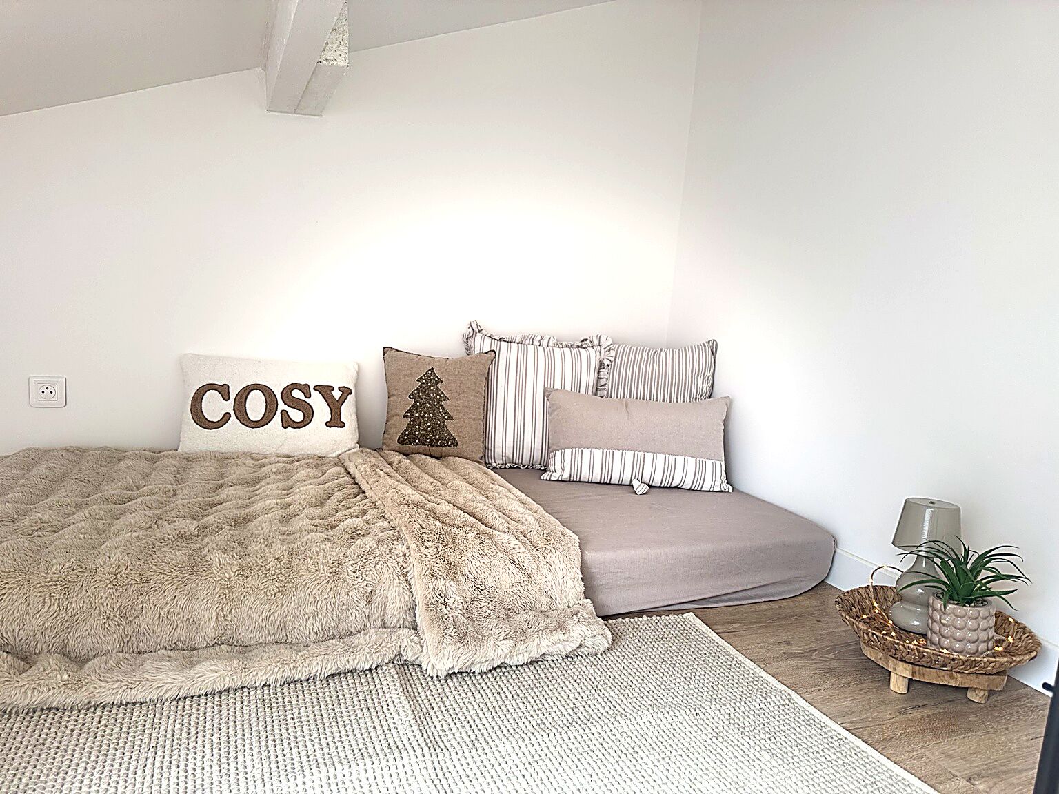 Een slaapkamer met een bed, kussens, een nachtkastje met een lamp en een kleine plant.