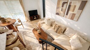 A living room with a sofa, coffee table, and chairs, a TV, and abstract wall art. - New cosy home & private garden -Near Paris - Free parking (Franconville)