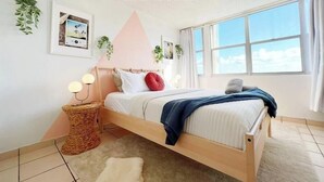 Une chambre à coucher avec un lit, une lampe de chevet, un tableau accroché au mur et une fenêtre.