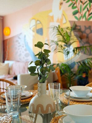 Een eettafel met helder glazen servies, een decoratieve vaas en een schilderij op de achtergrond.