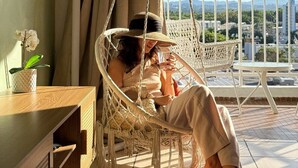 Une personne se détend dans un fauteuil suspendu sur un balcon, avec vue sur la ville.
