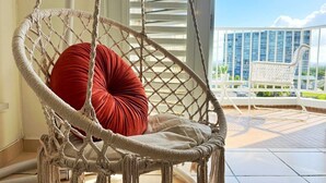 Une chaise en macramé avec un coussin rouge, une chaise blanche et un balcon offrant une vue sur les bâtiments.