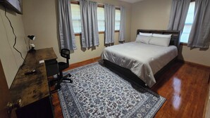 Une chambre à coucher comprenant un lit, un bureau, une chaise, un tapis et un ventilateur de plafond.