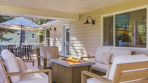 Un patio couvert avec un foyer extérieur, des sièges et une vue sur une maison.