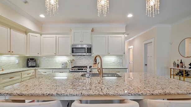 A modern kitchen with white cabinetry, granite countertops, stainless steel appliances, and a central island with bar stools.