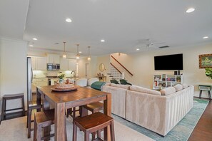 Ein modernes Wohnzimmer mit einer Eckcouch, einem Esstisch mit Stühlen, einer Küchenzeile und einer Treppe.