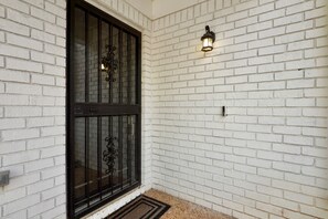 Une façade en briques blanches, une porte en métal noir et un luminaire fixé au mur.