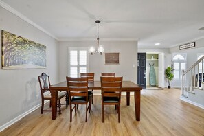 Un comedor con una mesa y sillas de madera, una araña y un cuadro en la pared.