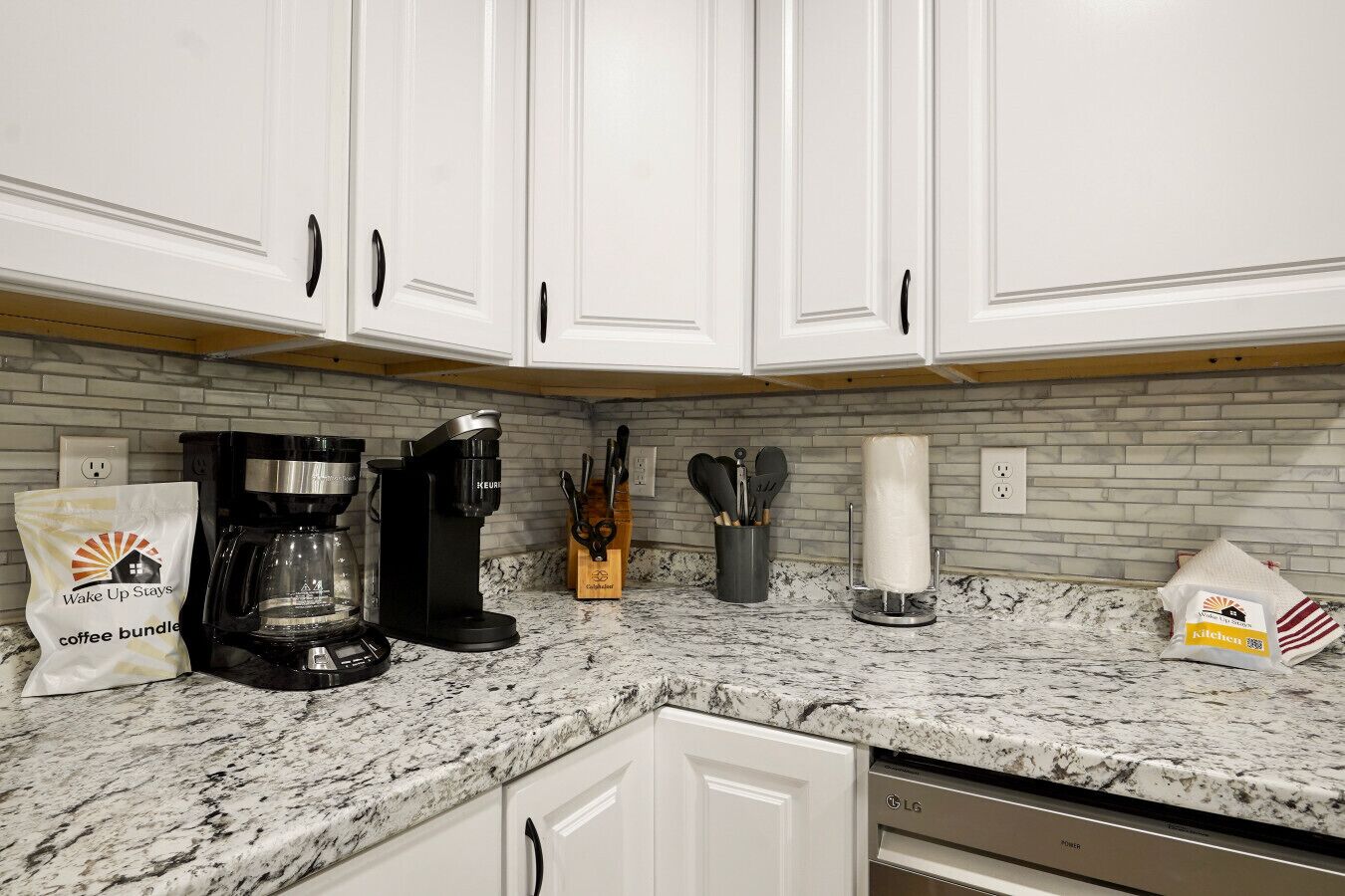 A kitchen with white cabinets, a coffee maker, a knife block, a paper towel holder, and a bag of coffee.