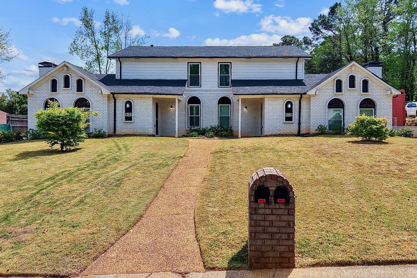 A large, two-story white brick house with a symmetrical facade, multiple windows, and a central entrance.