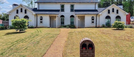 A large, two-story white brick house with a symmetrical facade, multiple windows, and a central entrance.