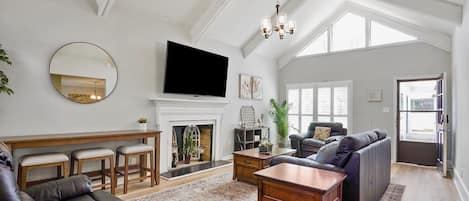 A spacious living room with a fireplace, a television, and a high ceiling with skylights.