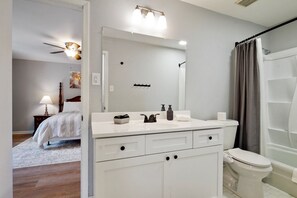Un baño con lavamanos blanco, espejo, inodoro, cortina de ducha y ventilador de techo.