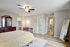 Ein Schlafzimmer mit Bett, Schminktisch, Spiegel, Deckenventilator und einem Flur zu einem anderen Raum.