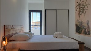 Ein Schlafzimmer mit Bett, Nachttisch mit Lampe, einer Tür mit Blick und einem Bild an der Wand.
