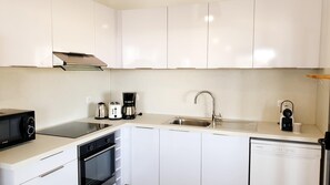 Eine moderne Küche mit weißen Schränken, einer Edelstahl-Dunstabzugshaube, einem Backofen, einem Geschirrspüler, einer Spüle mit Wasserhahn und einer Kaffeemaschine.