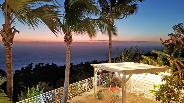 Ett område vid poolen med solstolar, en pergola och utsikt över havet i skymningen.
