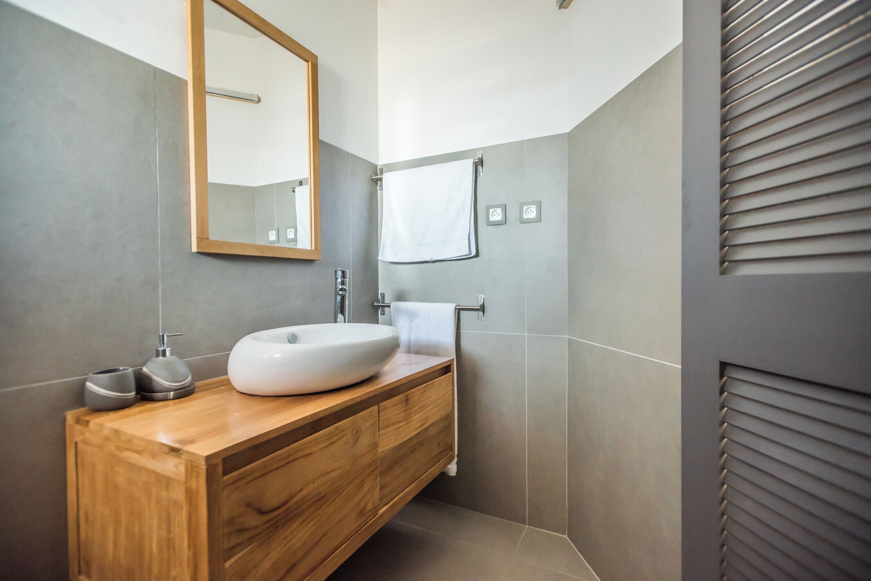 Een moderne badkamer met een houten wastafelmeubel, een witte wasbak en een spiegel.