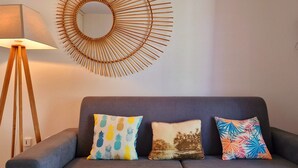 A grey sofa with three decorative pillows, a floor lamp, and a sunburst mirror on the wall.