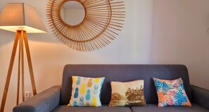 A grey sofa with three decorative pillows, a floor lamp, and a sunburst mirror on the wall. - Appartement Le Bel avec terrasse, incredible sea view and pool space (Petite Île)