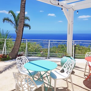 A terrace with white chairs and a table, overlooking a coastal view. - Appartement Le Bel avec terrasse, incredible sea view and pool space (Petite Île)