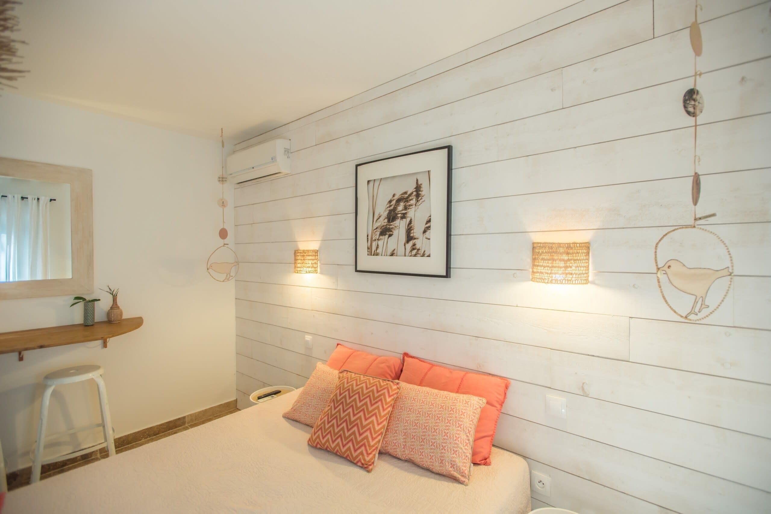 Un dormitorio con cama, almohadas, estante en la pared, lámpara colgante y un cuadro enmarcado.
