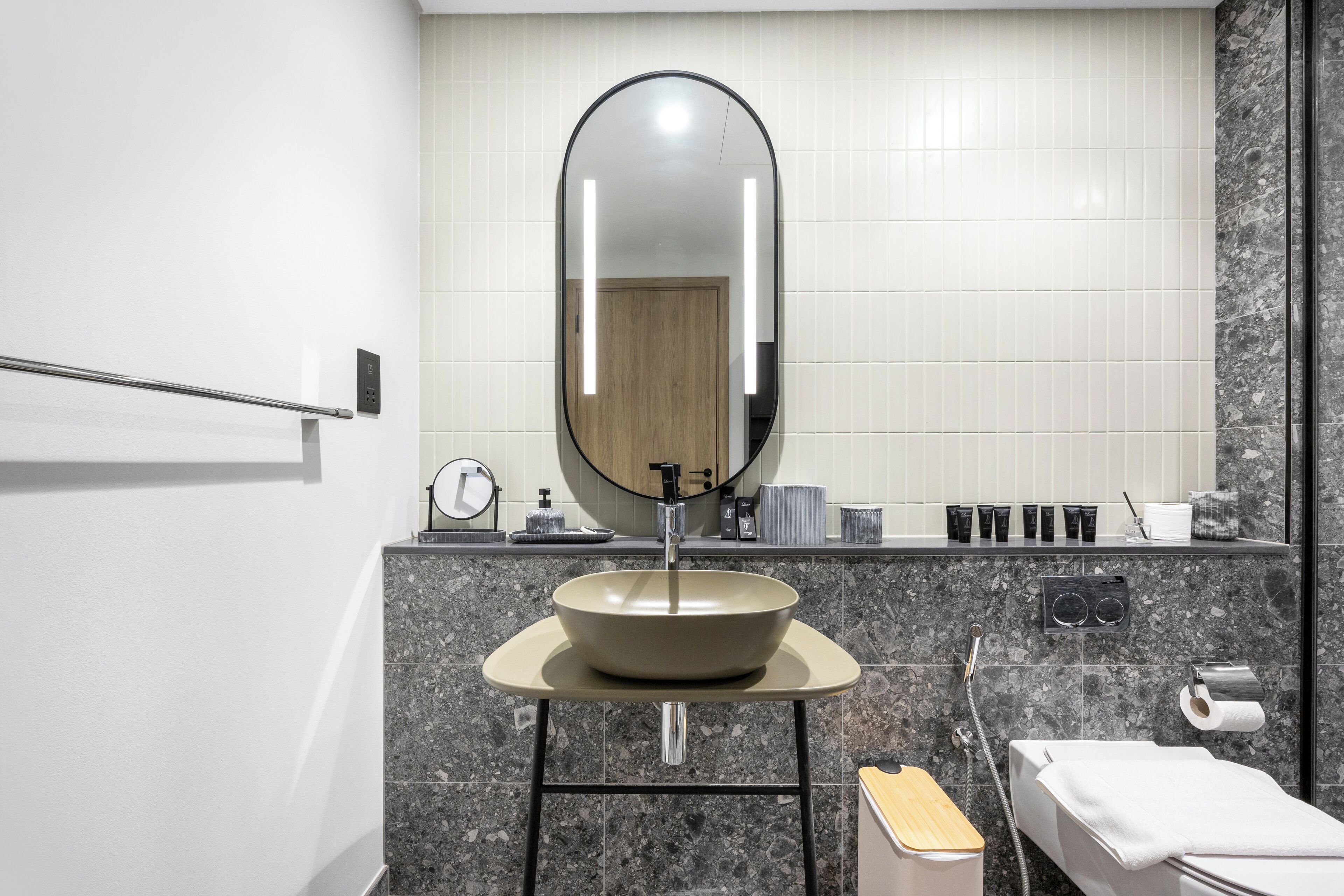 Een moderne badkamer met een ronde spiegel, een wastafel, een handdoekhouder en een toiletpapierhouder.