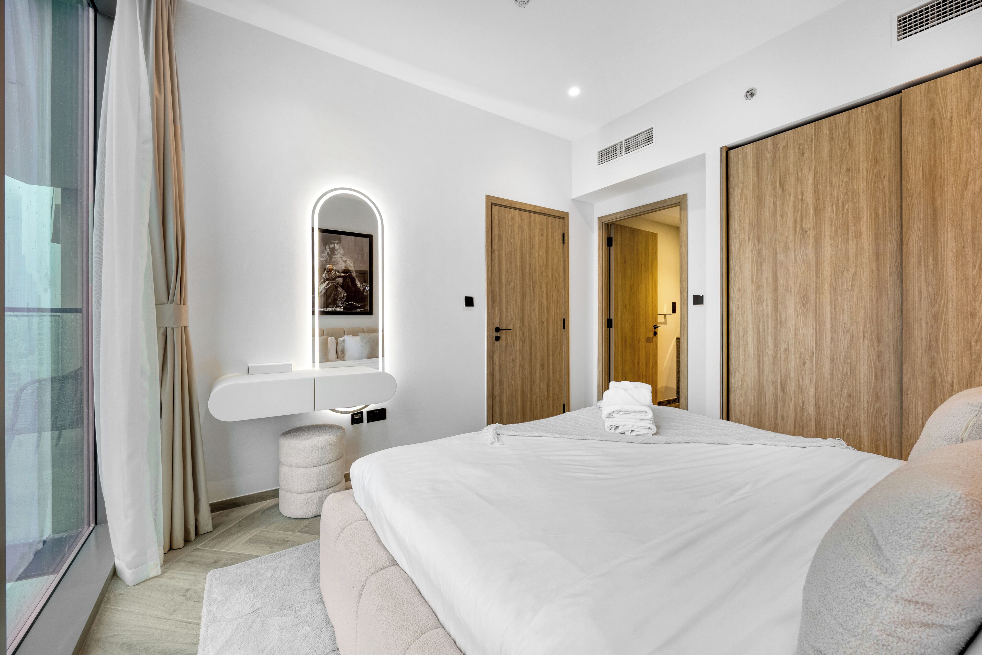 Een moderne hotelkamer met een groot bed, nachtkastje, spiegel, kledingkast en raam met gordijnen.