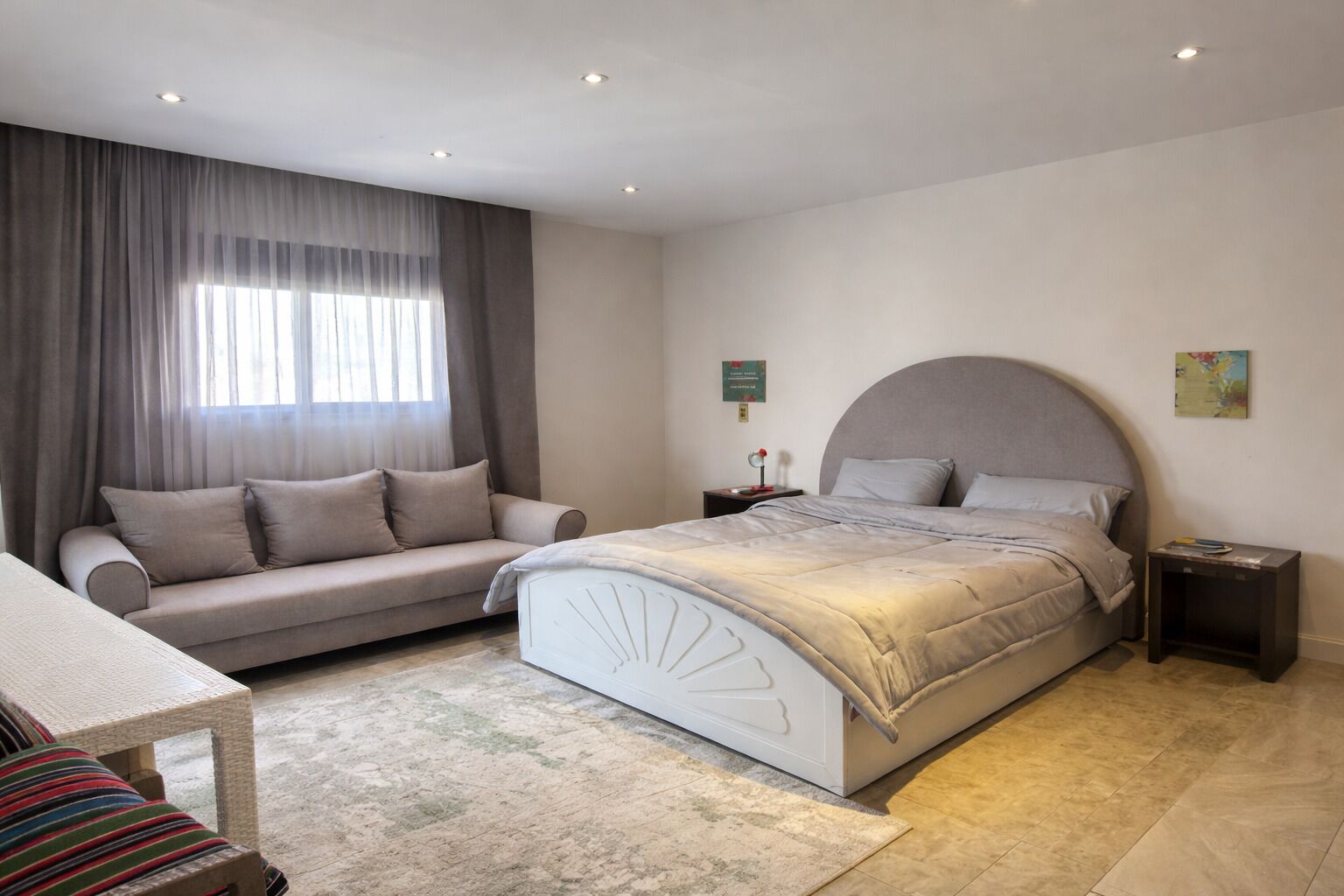 A bedroom with a bed, a sofa, a nightstand, and a window with curtains.