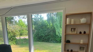 Una sala de estar moderna con un ventanal grande, un sillón de cuero negro, una mesita de madera y un jarrón con flores.