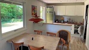 Un comedor con mesa y sillas de madera, una cocina con armarios blancos y una ventana con vista a zonas verdes.