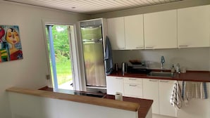 Cocina moderna con armarios blancos, refrigerador de acero inoxidable, encimera de madera y vistas a zonas verdes.