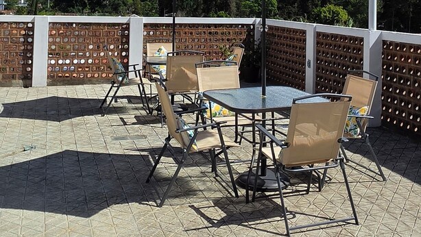 Een terras buiten met tafels en stoelen, een bakstenen muur en een berg op de achtergrond.