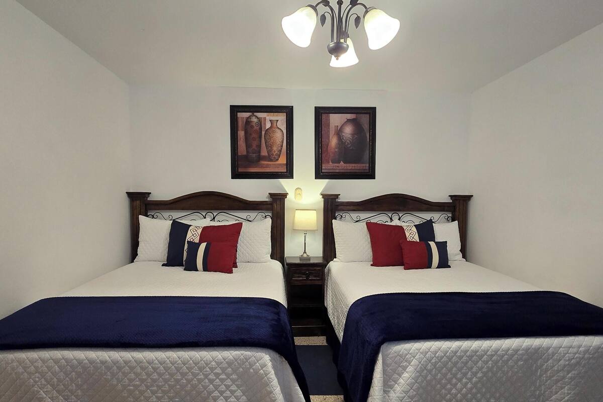 Habitación de hotel con dos camas, una araña y dos cuadros en la pared.