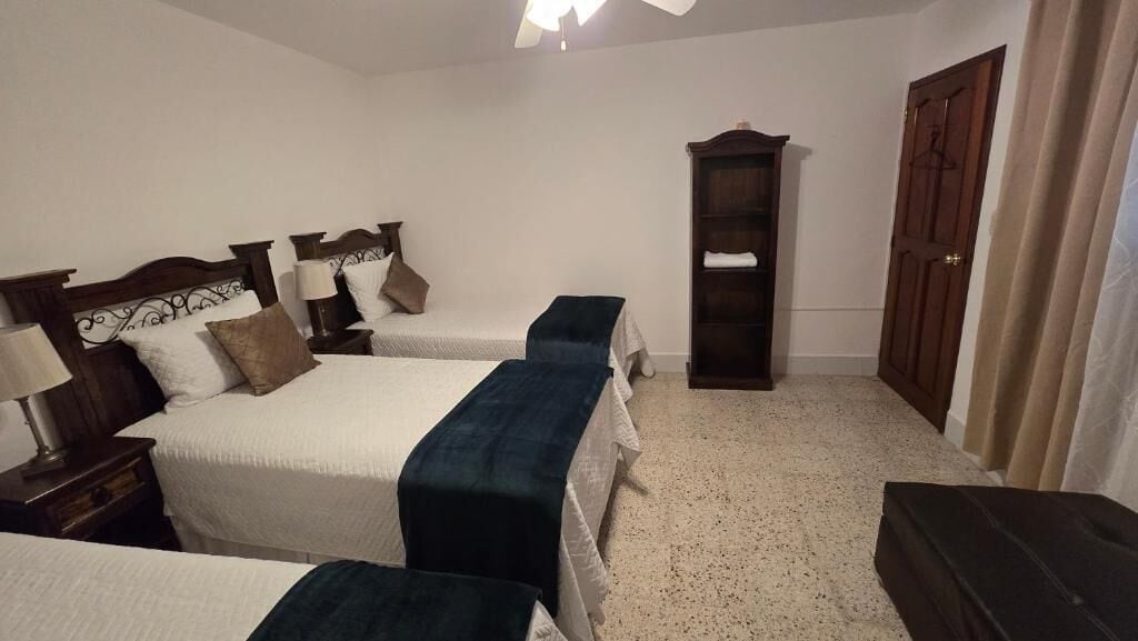 Un dormitorio con dos camas, un armario, una mesita de noche con lámpara y suelo cubierto de alfombra.