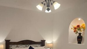 Een slaapkamer met een bed, een nachtkastje, een wandplank met bloemen en een plafondlamp.