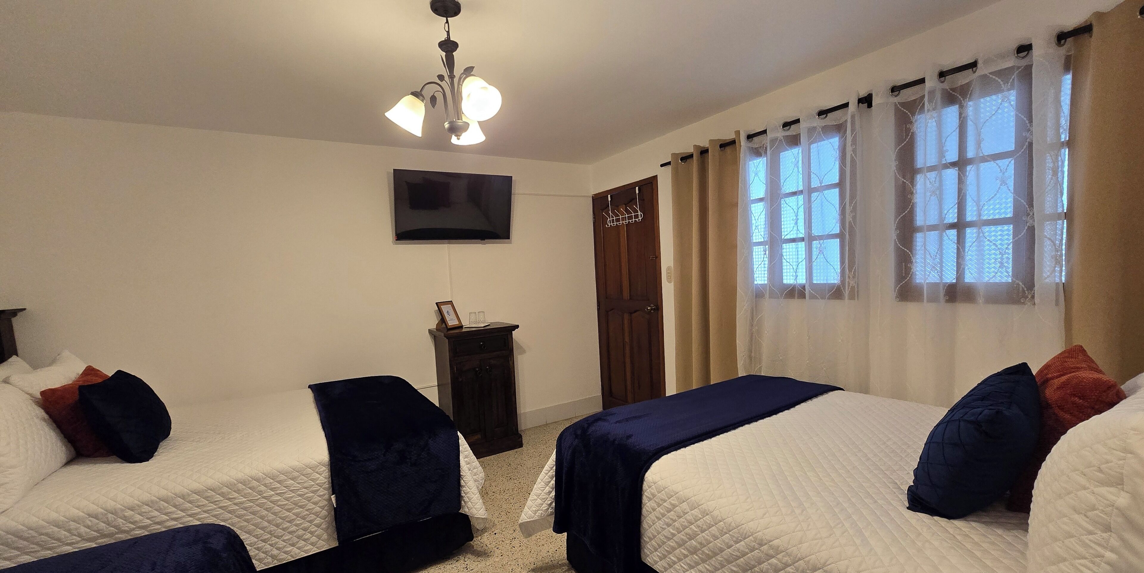 A hotel room with two beds, a TV mounted on the wall, a small cabinet, and a door with a coat rack.